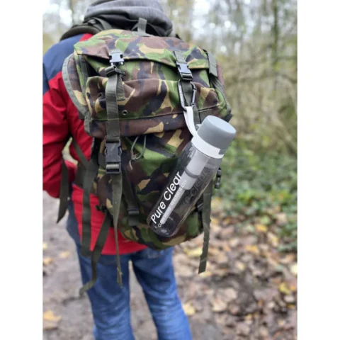 Active water filter bottle by Pure Clear attached to a camouflage backpack, set in a natural outdoor environment.