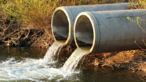 Concrete pipes discharging murky water into a river, highlighting water contamination issues related to the cryptosporidium outbreak in Devon.