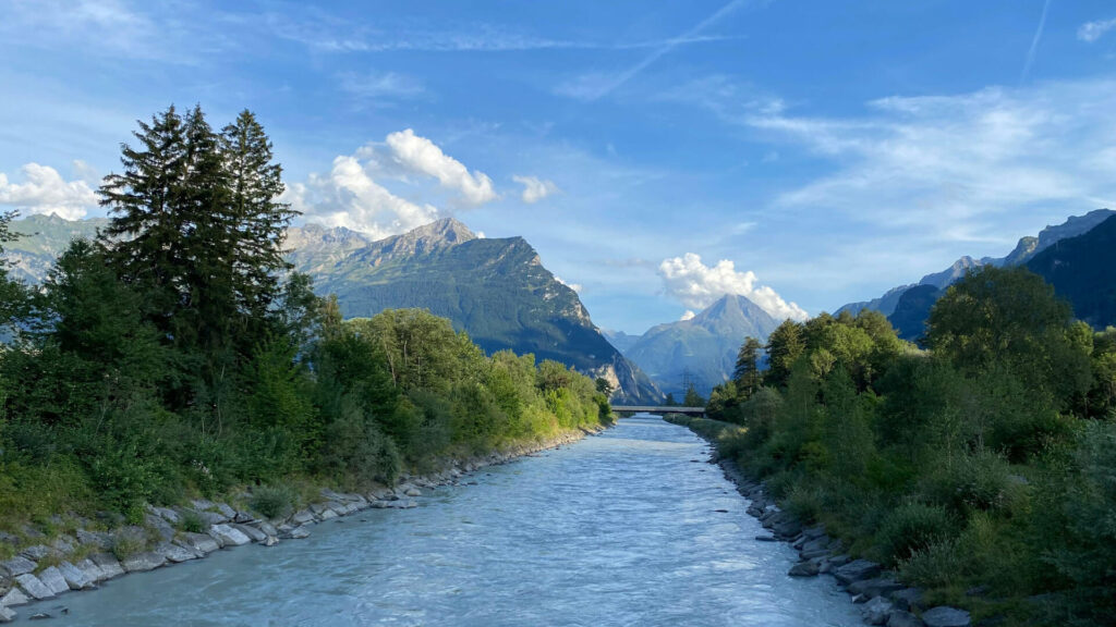 River flowing through lush greenery with mountains in the background, illustrating the natural environment and sustainability focus of Pure Clear Filters' recycling programme.