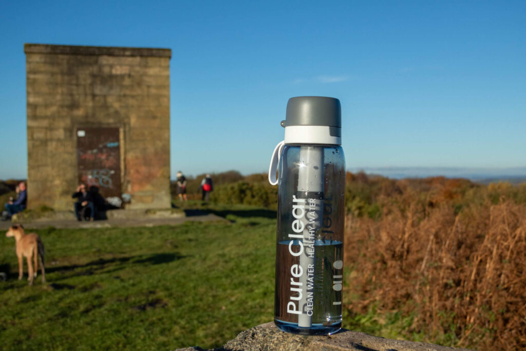 Pure Clear water bottle in outdoor setting with people and a stone structure in the background, emphasizing healthy hydration solutions.