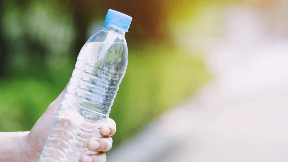Hand holding a clear plastic bottled water against a blurred natural background, illustrating the environmental impact of single-use plastic bottles.