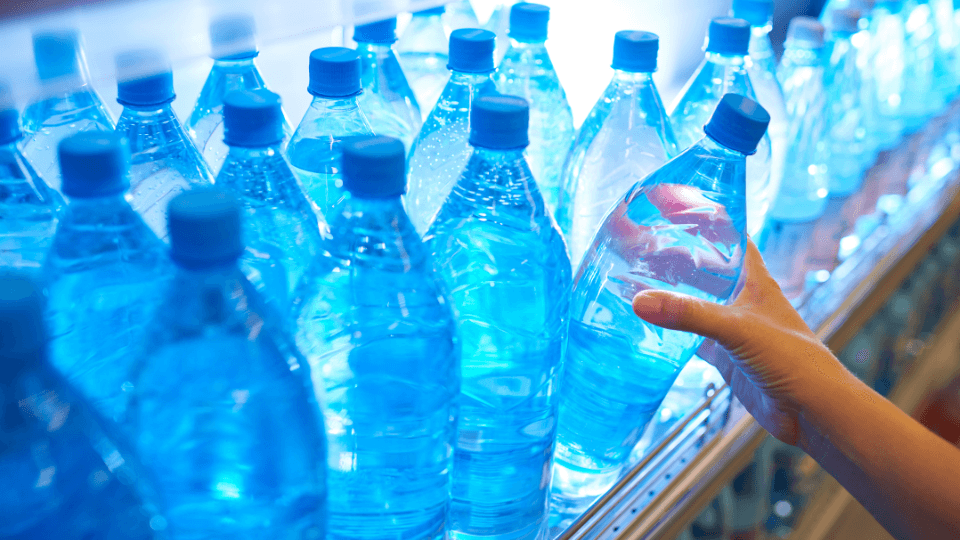 Hand reaching for a plastic bottled water among rows of blue water bottles, highlighting concerns about bottled water quality and contamination.